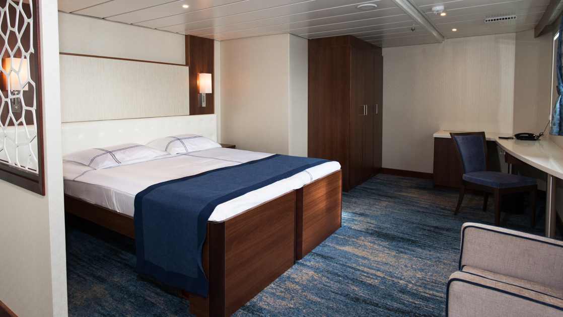 Owner's Suite on G Expedition ship with double bed in blue & white linens, padded white headboard, gray chair & desk.