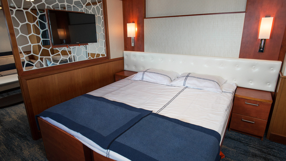 Suite Double on G Expedition ship with double bed in blue & white linens, padded white headboard & TV on latticed window.