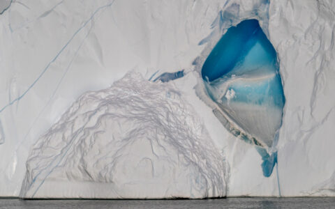 White face of a glacier with a bright blue cave meets calm sea, seen on a Greenland: Disko Bay cruise in the Arctic.
