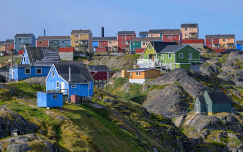 Green hillside with colorful small homes under a blue sky, seen on the Greenland: Disko Bay & Ilulissat cruise in the Arctic,