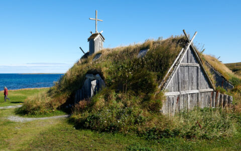 Greenland to East Canada cruise guest walks past massive historic church built of aging wood with a living roof in Canada.