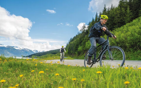 cyclist biking through the green grass fields of Alaska off of a small ship cruise on a sunny day