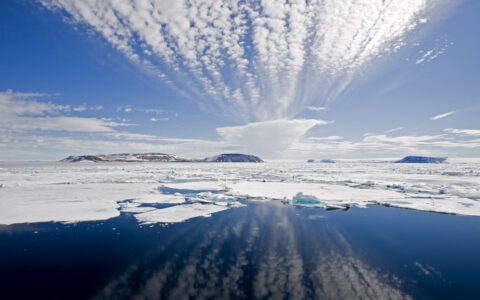 Edge of pack ice in large & small chunks with cloud reflections on glassy water during a sunny day near Iceland.
