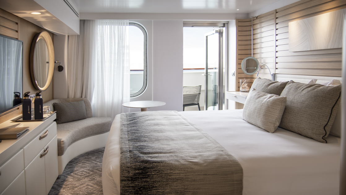 Deluxe Stateroom aboard Le Bellot French ship, with king bed, white dresser, small couch, private balcony, chair & chic decor.