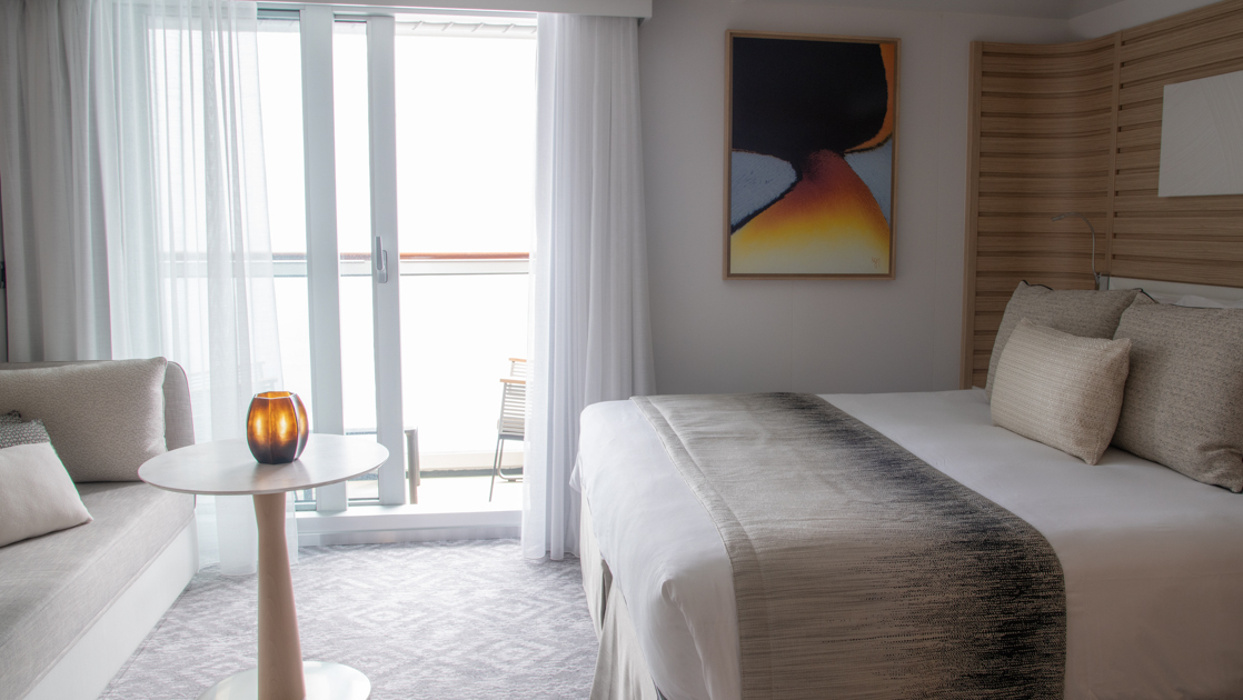 Deluxe Suite aboard Le Bellot French luxury expedition ship, with king bed, small table, couch, private balcony & chic decor.
