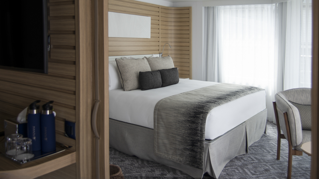 Grand Deluxe Suite aboard luxury french ship Le Bellot, with ethnic chic decor, wooden headboard, king bed & separate living room.