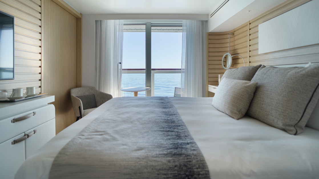 Prestige Suite aboard Le Bellot French small ship, with chic decor, white linen king bed, private balcony, wooden walls, desk & chair.