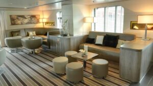 Interior of Le Boreal luxury French expedition ship, with tan couches, wooden coffee tables & wraparound windows.
