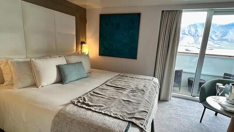 Deluxe Suite aboard Le Boreal expedition ship, showing king bed, table, chair & white-&-teal appointments.