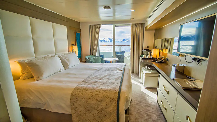 Prestige stateroom aboard Le Boreal expedition ship, showing king bed, desk & white-&-teal appointments.
