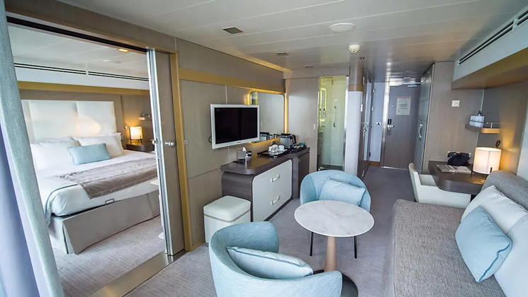 Prestige Suite for Decks 4, 5 & 6 aboard Le Boreal expedition ship, showing king bed, table, TV, chairs & white-&-teal appointments.