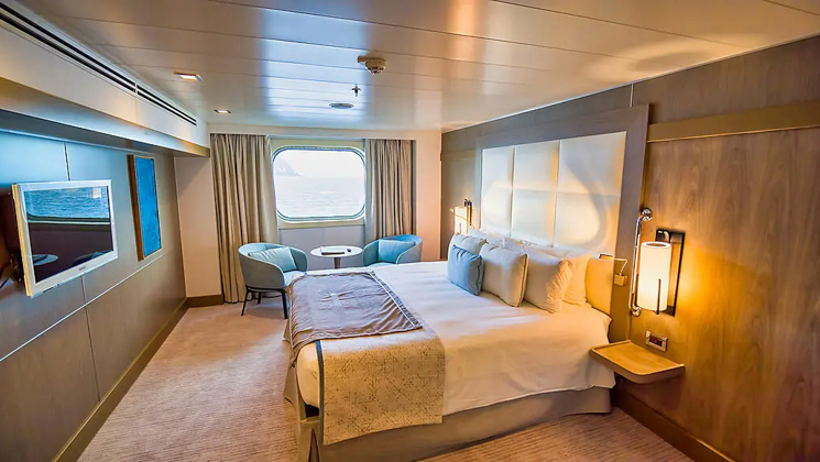Superior stateroom aboard Le Boreal expedition ship, showing king bed, table & chairs, window & white-&-teal appointments.