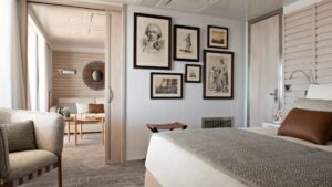 View from bedroom to window-lined living room with couch in the beige-accented Owner's Suite on Le Bougainville cruise ship.