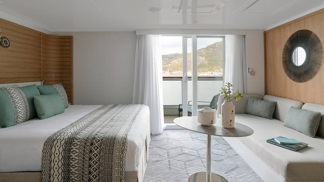 Deluxe Suite aboard Le Champlain French luxury expedition ship, with king bed, small table, couch, private balcony & ethic-chic decor.