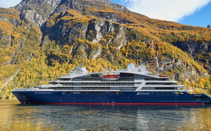 Le Champlain, luxury expedition ship with a red, blue & white exterior, sits in front of cascading waterfalls.