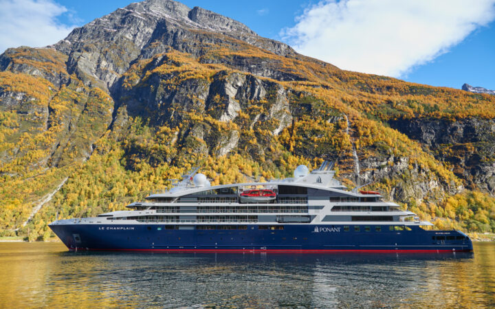 Le Champlain, luxury expedition ship with a red, blue & white exterior, sits in front of cascading waterfalls.