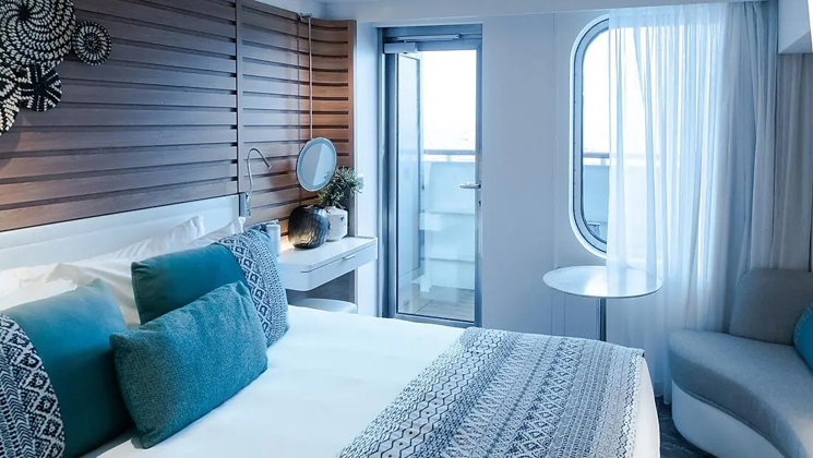 Deluxe Stateroom aboard Le Champlain French ship, with king bed, door to private balcony, small couch & ethnic-yet-chic decor.