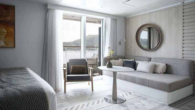Deluxe Suite aboard Le Dumont D'Urville French luxury expedition ship, with king bed, small table, couch, private balcony & ethinc-chic decor.