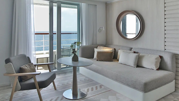 2nd room of Privilege Suite aboard French luxury ship Le Dumont D'Urville, withcouch, table, chair & private balcony, plus natural-looking decor.