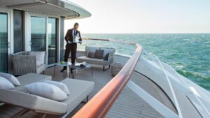 Server in formal wear & white gloves delivers a chilled bottle of champagne to an empty deluxe suite terrace of Le Jacques Cartier French ship as she sails in open waters.