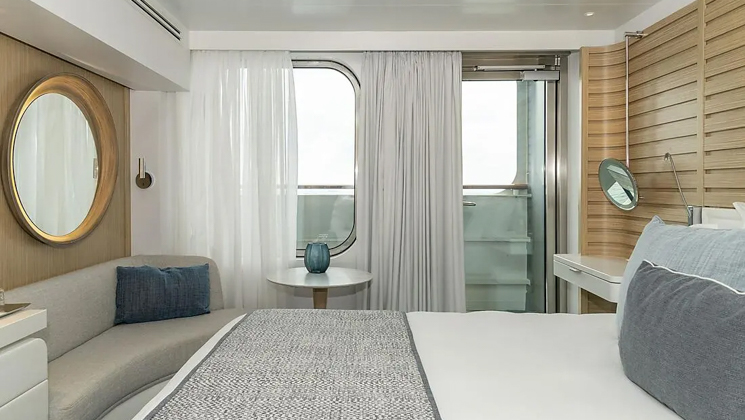 Deluxe Stateroom aboard Le Jacques Cartier French ship, with king bed, white dresser, door to private balcony, desk & ethnic-yet-chic decor.