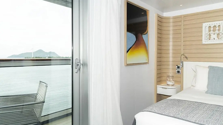 Deluxe Suite aboard Le Jacques Cartier French luxury expedition ship, with king bed, ethnic-chic decor & sliding glass door to private balcony.