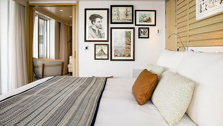 Owner's Suite aboard Le Jacques Cartier luxury expedition ship, showing king bed, separate living room, bright white decor & photos & drawings of explorers on the walls.