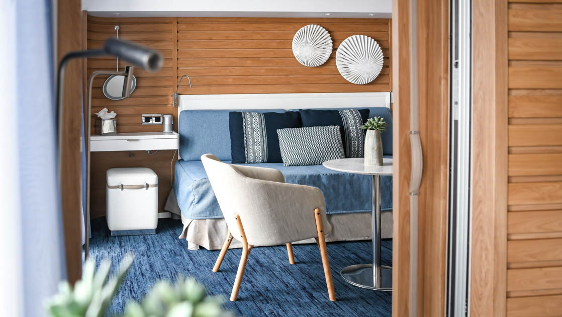 View from bedroom into Prestige Suite second room lounge with sofa bed, coffee table, chair & wood walls on Le Laperouse.