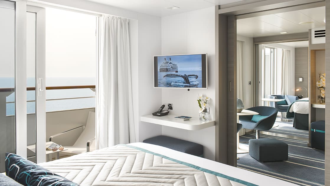 Grand Privilege Suite aboard luxury expedition ship Le Lyrial, in blue-&-white decor with king bed, TV, private balcony, desk, separate living room & second bedroom.