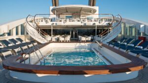 Pool deck aboard Le Lyrial luxury ship, with long swimming pool surrounded by chaise loungers & 2 wrapping staircases that lead to an overview terrace.