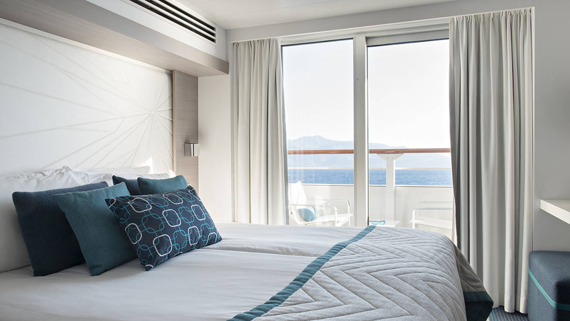 Prestige Stateroom aboard French expedition ship Le Lyrial, with king bed, blue-&-white decor, desk & private balcony.