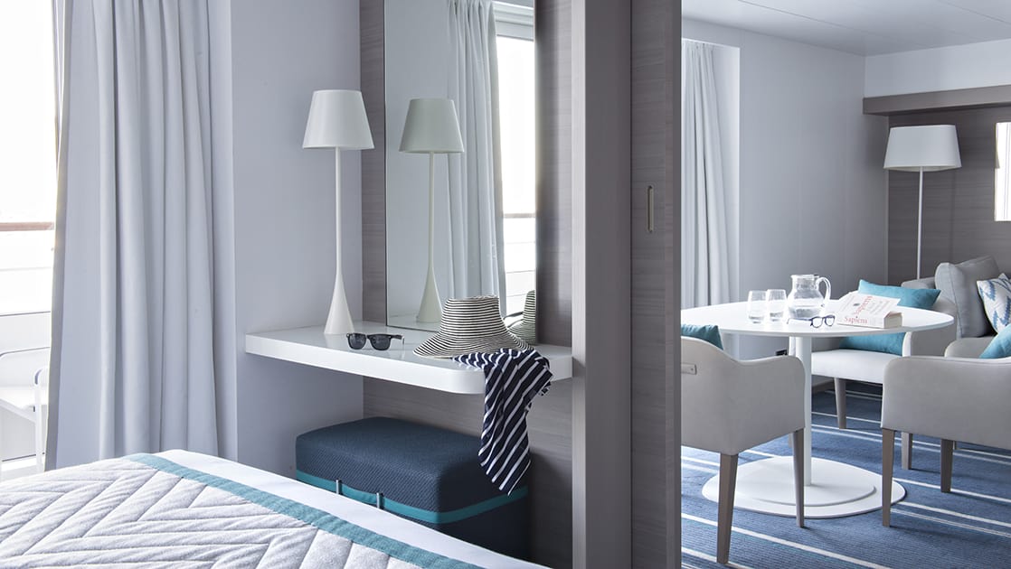 Privilege Suite on Le Lyrial French expedition ship, with king bed, desk, mirror, separate room with table & chairs & blue-&-ivory decor.