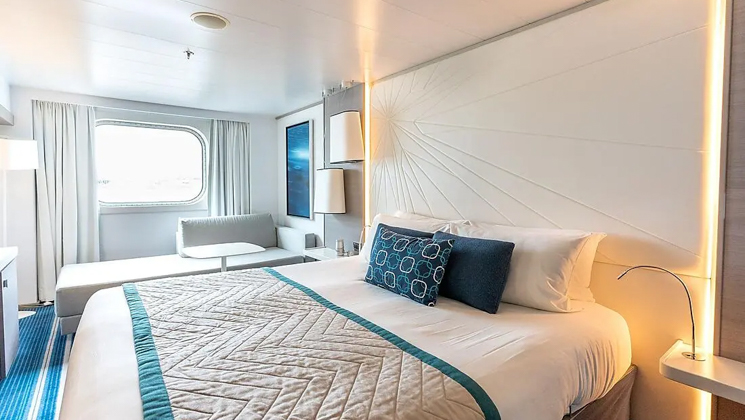 Superior Stateroom aboard Le Lyrial French luxury ship, with bed, bedside table, reading light, lamp, window & blue-&-white decor.