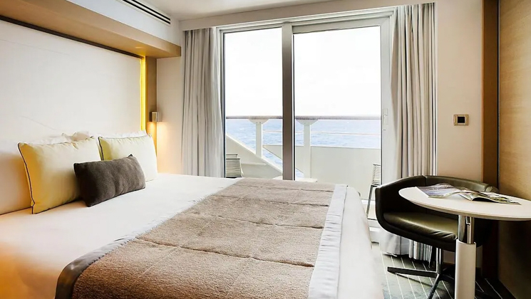 Prestige Stateroom aboard Le Soleal with king bed. A tall white headboard, brown & beige pillows & private balcony.