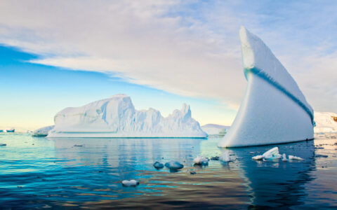 Large, skinny, rounded iceberg rises like a wall out of calm turquoise water, seen on the Nat Geo White Continent cruise.