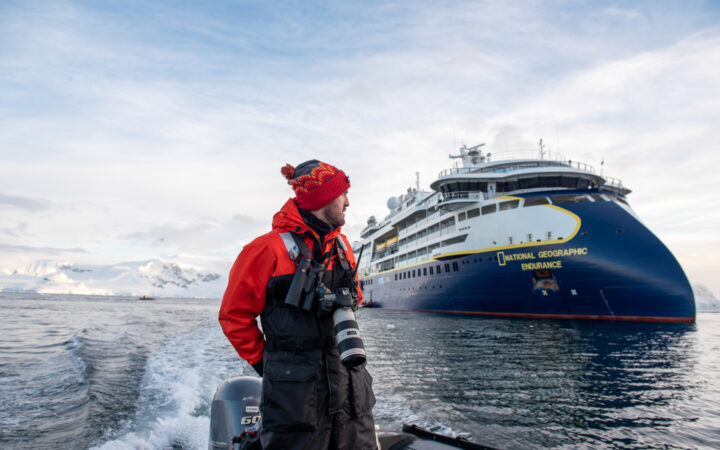 man standing on zodiac driving away from National Geographic Endurance in Foyn Harbour, Antarctica.