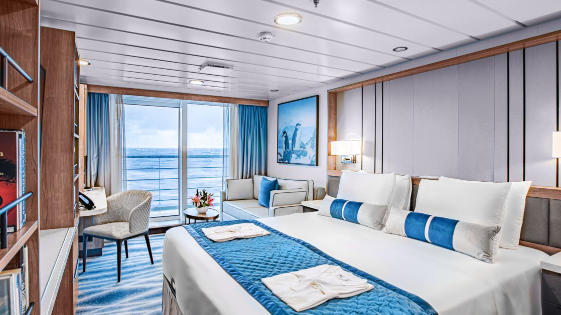 A modern cabin on the MS Ocean Victory cruise ship with a large bed, a desk, and a balcony.