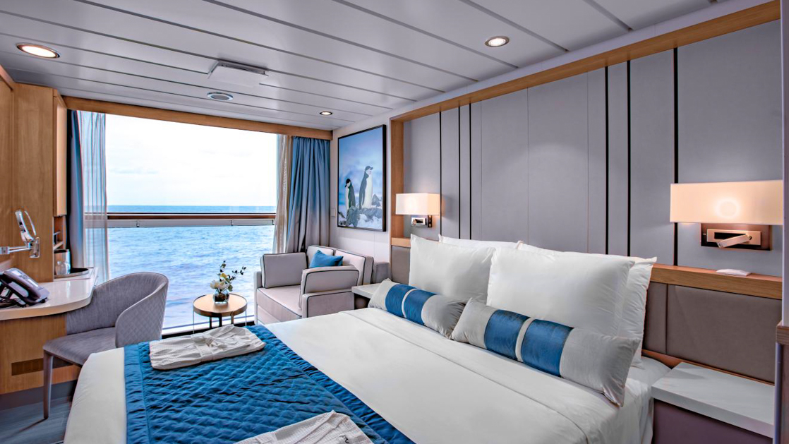 A modern, well-appointed cabin on a cruise ship with a large bed, a window with an ocean view, and contemporary decor.