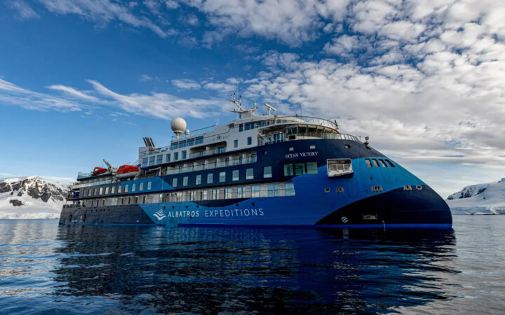 blue and white polar expedition ship Ocean Victory cruising through the icy waters of Antarctica on a sunny calm day