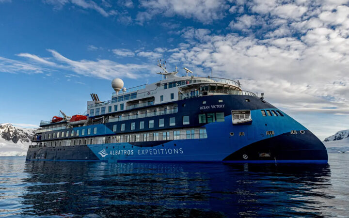 blue and white polar expedition ship Ocean Victory cruising through the icy waters of Antarctica on a sunny calm day