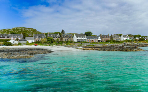 Teal sea beside small town with gothic architecture under a blue sky in Scotland.