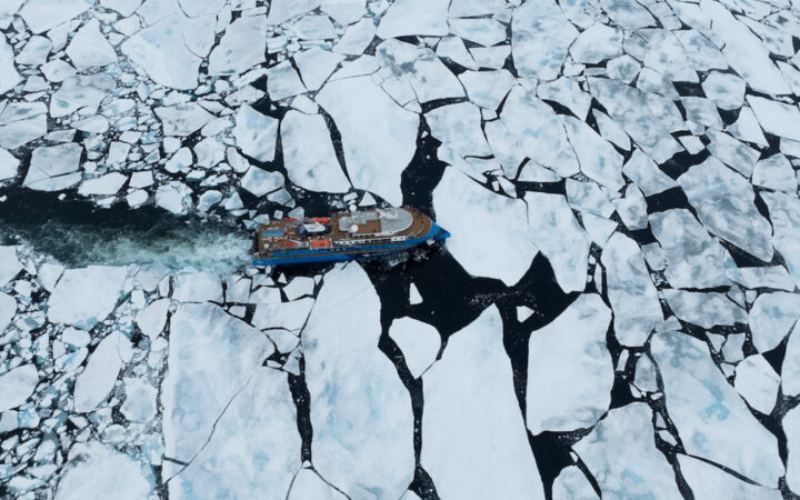 Aerial view of modern blue small ship with teak top deck cruising through pack ice on a Svalbard cruise in the Arctic.