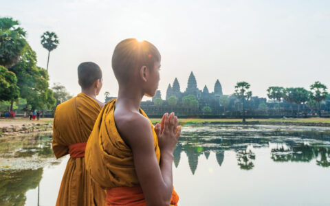 Two young monks at Angkor Wat, temple complex, in Cambodia overlooking calm waters and green trees