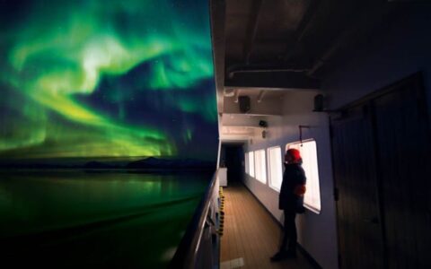 Green and blue northern lights illuminate the sky and the ocean just off the side of the ship for the arctic sights cruise