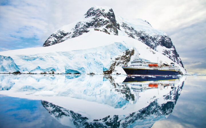 With water like glass the snow covered Antarctica landscape and National Geographic small ship have a perfect mirrored reflection