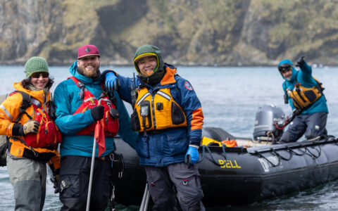adventurists in outdoor gear are possed for a picture getting off a small skiff off the water