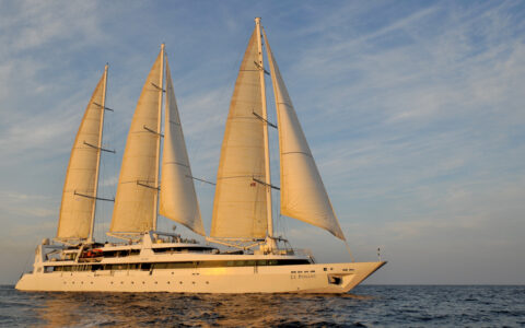 Motorsailor Le Ponant in white with 5 sails cruises calm sea in soft light at sunset on French Riviera cruises.