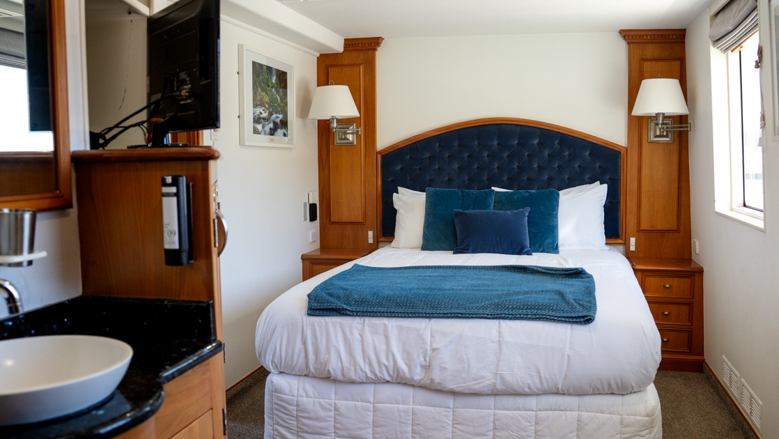 Royal Suite with double bed in blue & white with plush headboard & wood side table by view window on Heritage Explorer.