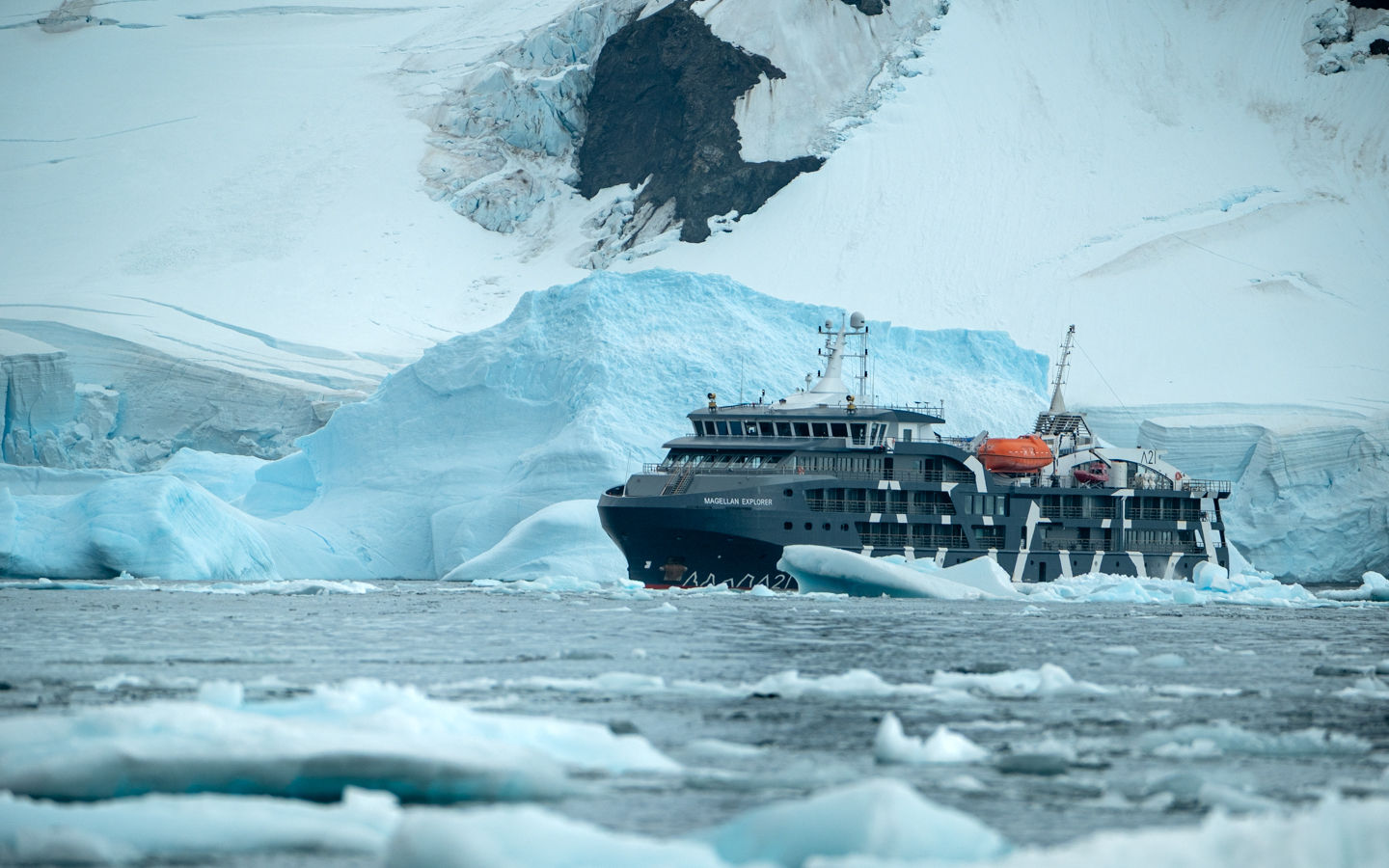 Expedition ship Magellan Explorer anchored in a bay in Antarctica with large sea ice floating by with mountainous terrain off in the distance