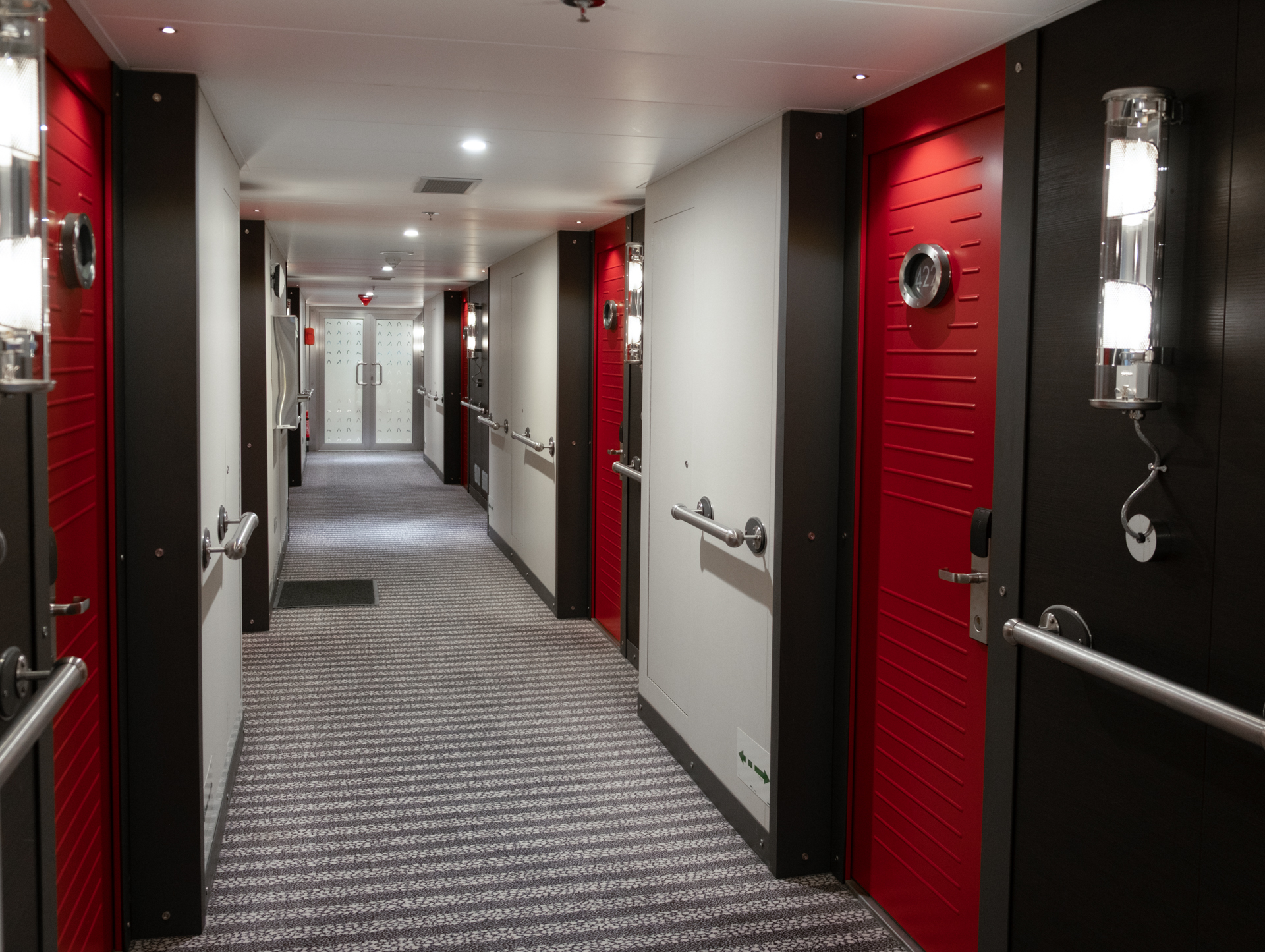 interior hallway of Magellan Explorer small polar ship. Red doors with striped grey and white carpet line the halls.